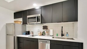 A modern kitchen with dark cabinets, a stainless steel refrigerator, a microwave, and a dishwasher.