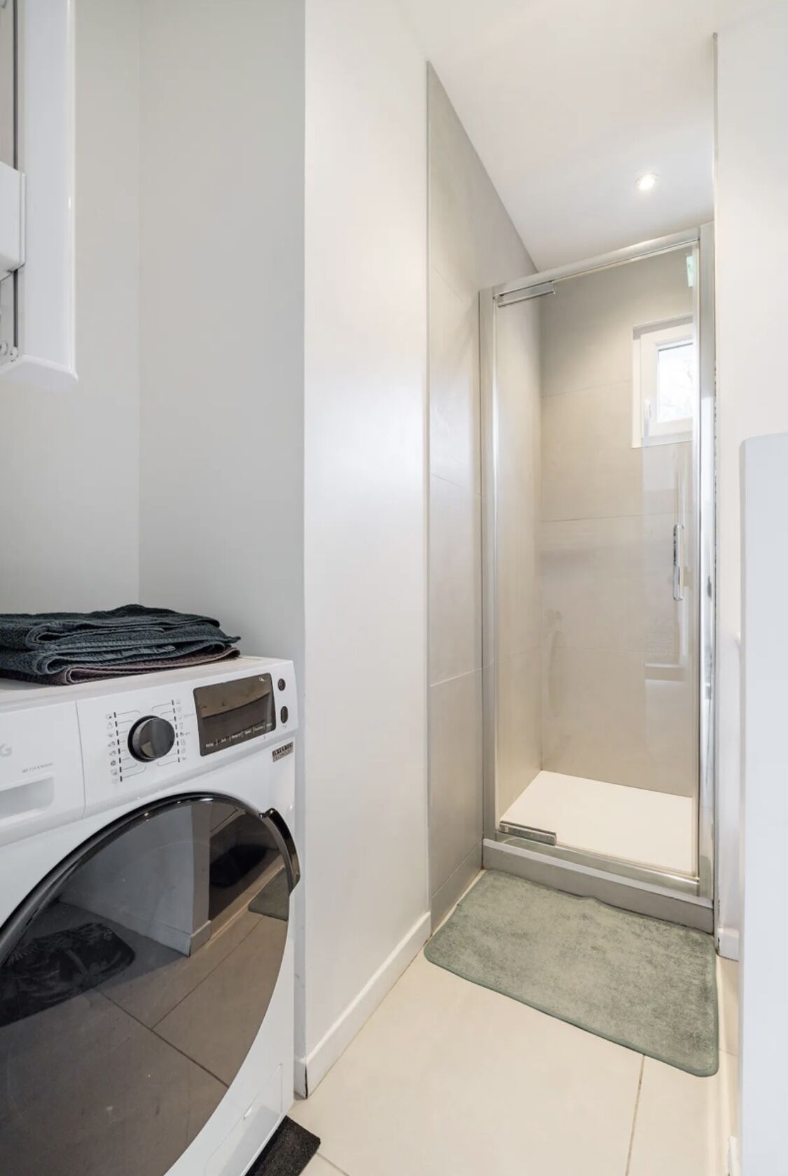 A compact laundry area with a washing machine and dryer, a glass shower enclosure, and a small rug on the floor.