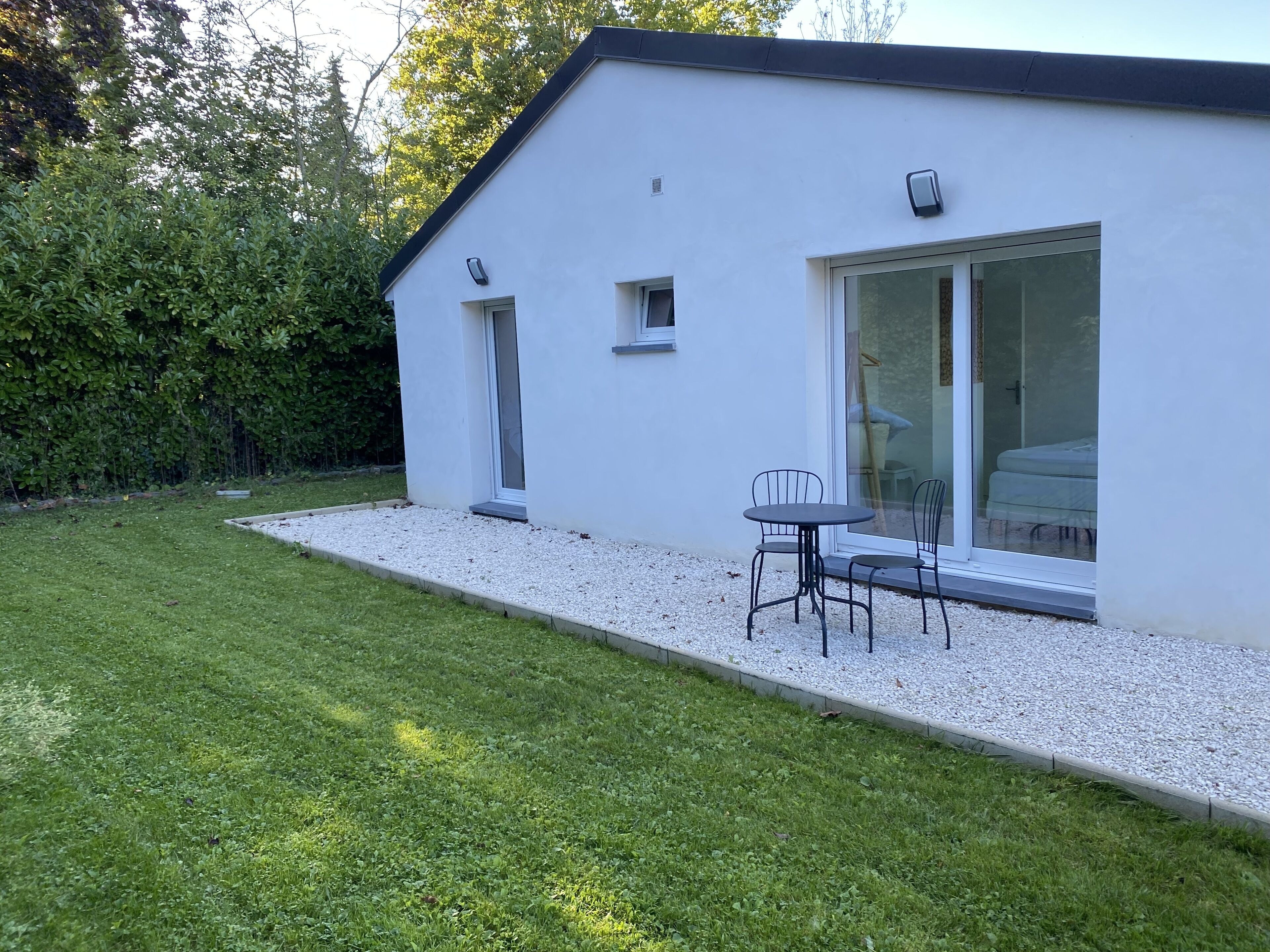 A modern house with a white exterior, a glass door leading to a patio area, and a small outdoor seating area with two chairs.