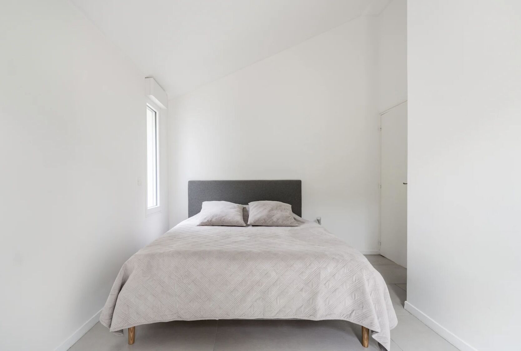 A minimalist bedroom with a bed, two pillows, and a window.