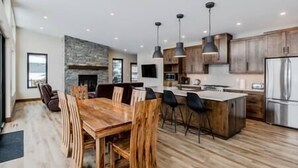 A modern kitchen with a central island, wooden dining table, and bar stools. - Luxury 4 BDR Home / Hot tub / Amazing Fireplace! (Fernie)