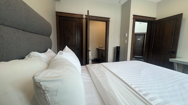 A hotel room with a large bed, a grey upholstered headboard, and wooden doors leading to a bathroom.