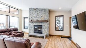 A modern living room with a stone fireplace, leather sofas, and a large window. - Luxury 4 BDR Home / Hot tub / Amazing Fireplace! (Fernie)