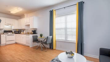 A modern kitchen with white cabinets, a dining area with a table and chairs, and a large window with yellow curtains.