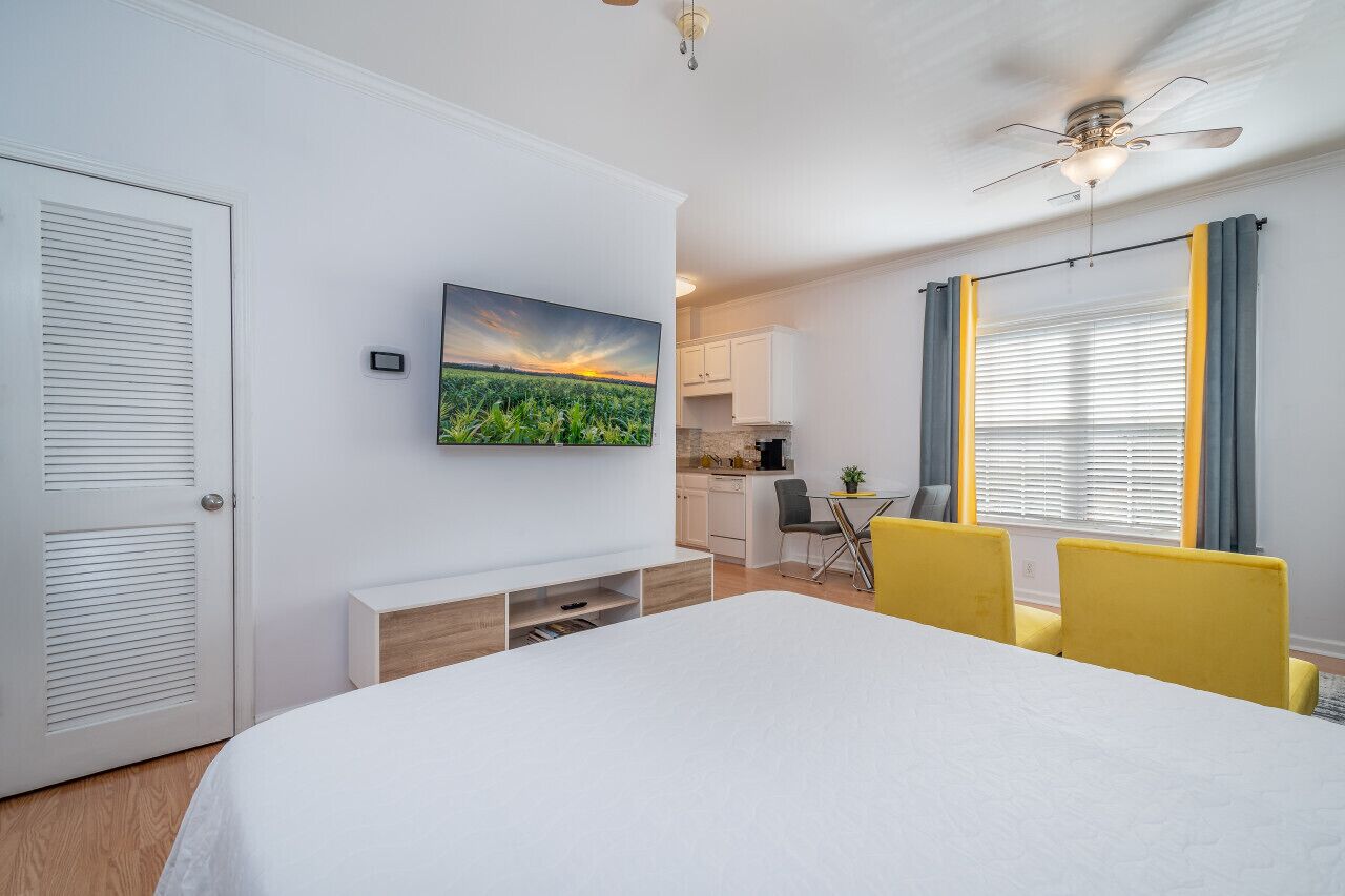 A bedroom with a bed, a TV mounted on the wall, a desk, and a chair.