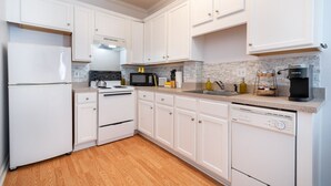 Una cucina moderna con mobili bianchi, un frigorifero in acciaio inossidabile, un forno a microonde, un fornello e una lavastoviglie.