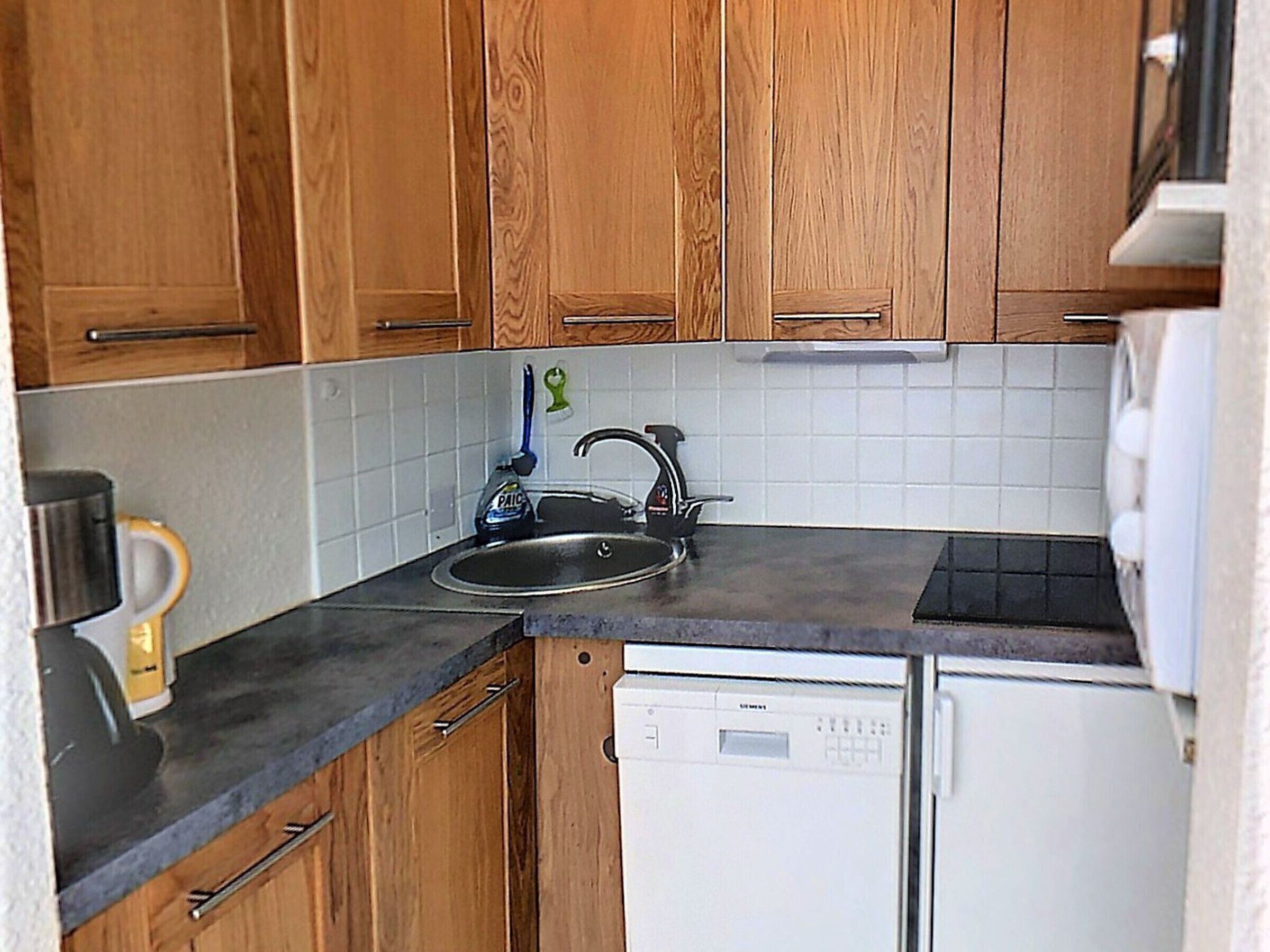 Une cuisine compacte avec des meubles en bois, un plan de travail noir, un évier, une machine à café et un lave-vaisselle.
