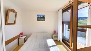 A bedroom with a bed, a bedside table, a nightstand, a mirror, and a window with a view of the countryside.