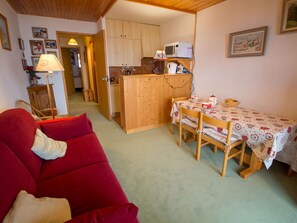 A cozy living room with a red sofa, a dining table with chairs, a kitchen area with wooden cabinets, and a microwave. - Cozy apartment near slopes with balcony (Méribel)