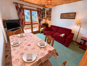 A furnished living room with a dining area, a red sofa, a television, and a table set for four.