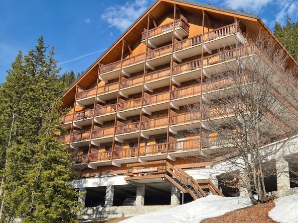 A multi-story wooden building with balconies, a sign reading 'Chandonelles 1', and a stone base.