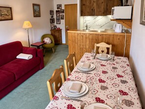 A cozy room with a red sofa, a dining table set with plates and glasses, a wooden cabinet, and a small table with a lamp.