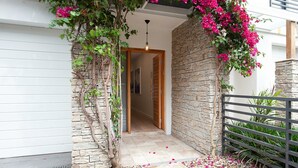 A modern entrance with a stone wall, a wooden door, and a hanging vine with pink flowers. - Bondi Coastal Charm ISYD (Bondi Beach)