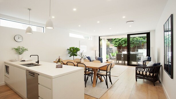 A modern kitchen with a central island, dining area with chairs, and a view of the outdoors through large sliding glass doors. - Bondi Coastal Charm ISYD (Bondi Beach)