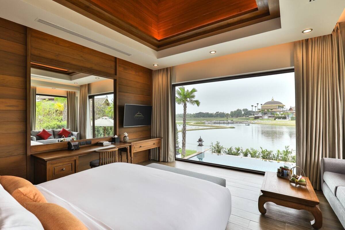 A hotel room with a large bed, a desk with a TV, and a view of a lake and buildings.