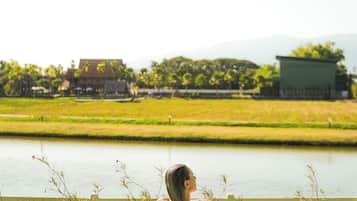 A person relaxing in a swimming pool with a view of a green field and a building in the background.