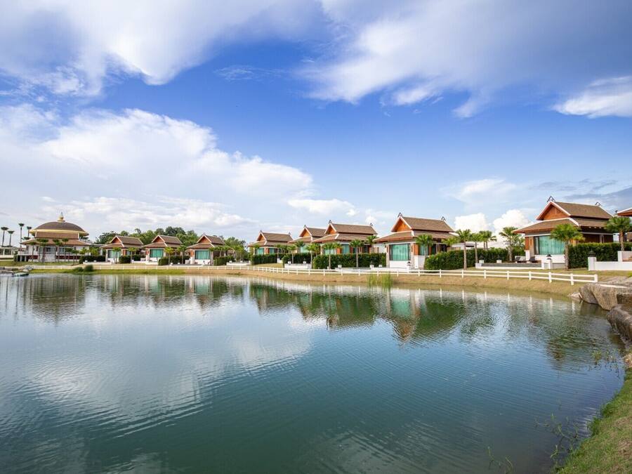Een rij traditionele villa's met een groot wateroppervlak op de voorgrond, waarin de gebouwen en lucht zich spiegelen.