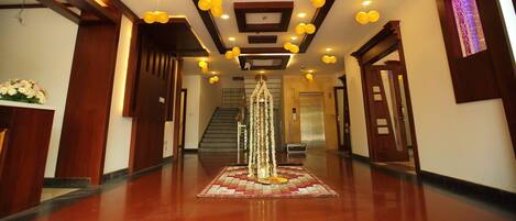 A hotel lobby with a polished wooden floor, a reception desk, and a staircase leading to an elevator.