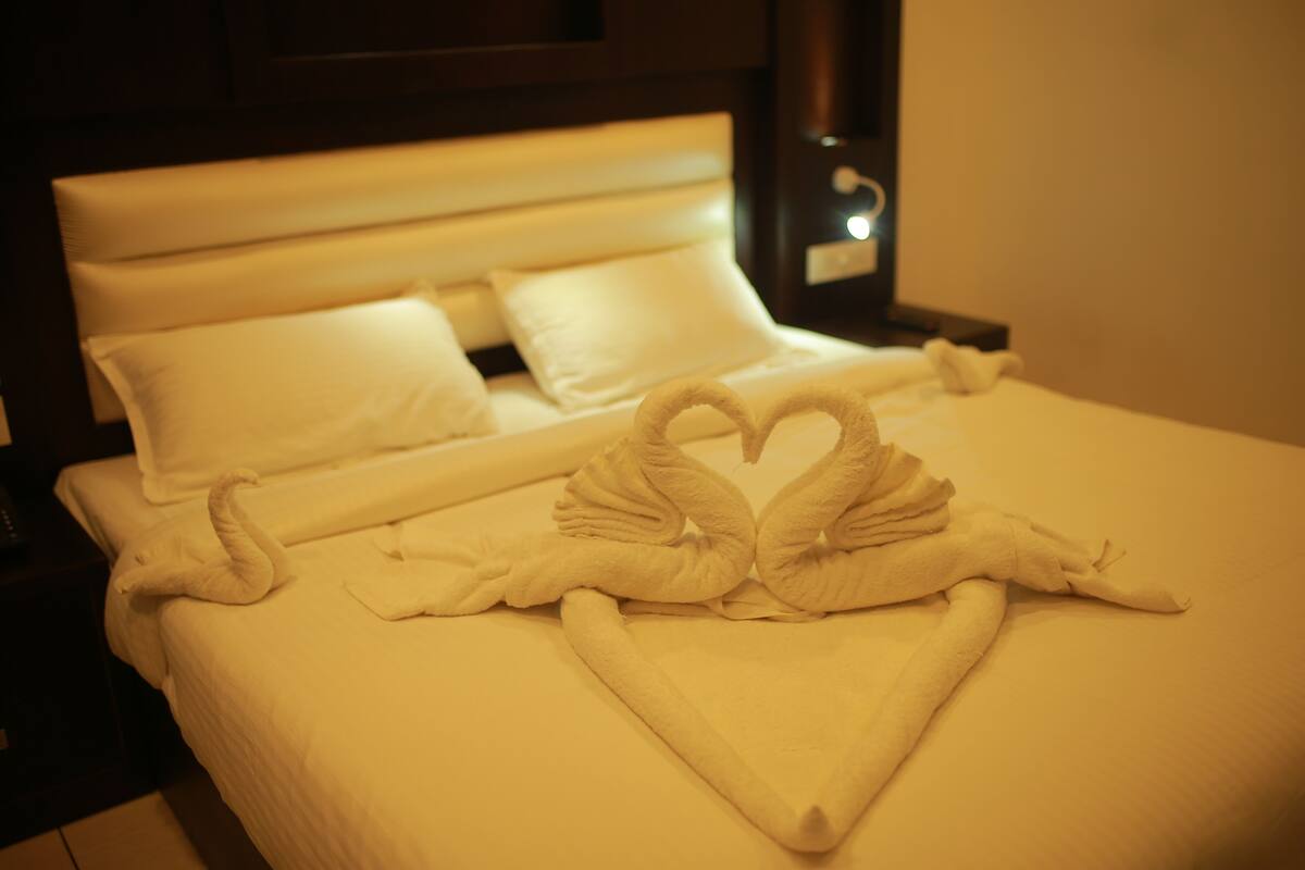 A neatly made bed with white linens and a heart-shaped towel arrangement.