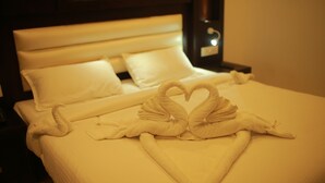 Un lit bien fait, avec du linge de lit blanc et une serviette pliée en forme de cœur.