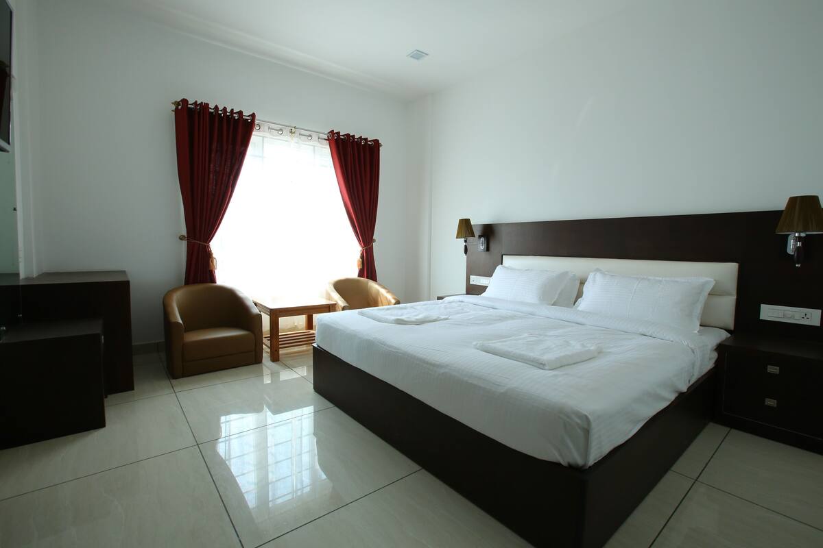 A hotel room with a large bed, a desk, a chair, and a window with curtains.