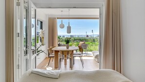 A room with a bed, a dining table with chairs, and a view of a grassy area and a road outside. - Gorgeous apartment in Kerteminde (Kerteminde)