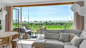 A spacious living room with a large sliding glass door leading to a balcony overlooking a green landscape. - Gorgeous apartment in Kerteminde (Kerteminde)