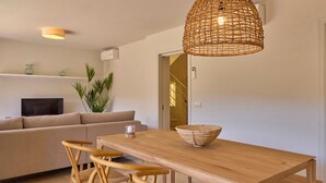 Een moderne woonkamer met een houten eettafel, rieten stoelen, een beige bank, een televisie en een grote geweven lamp.