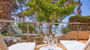 Een zonnig terras buiten met een tafel, twee lounge fauteuils en een glazen balustrade met uitzicht op een prachtig panorama.