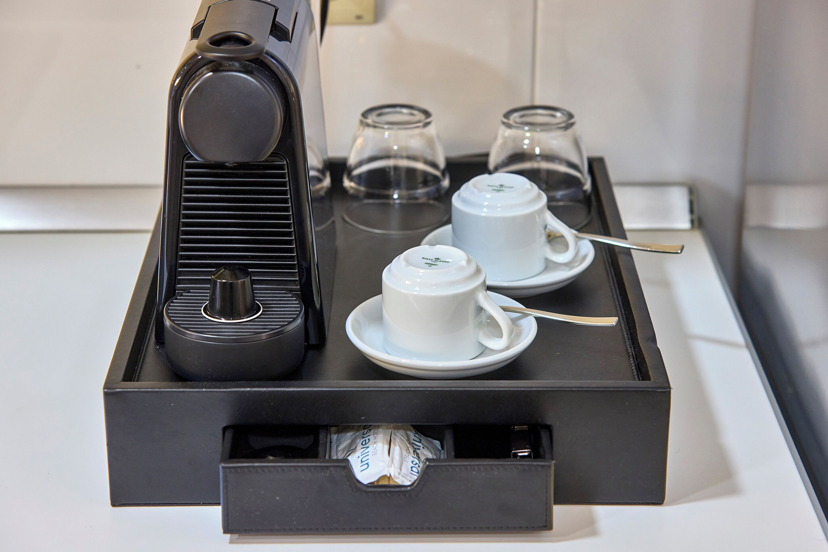 A coffee machine with two cups and two glasses on a tray.