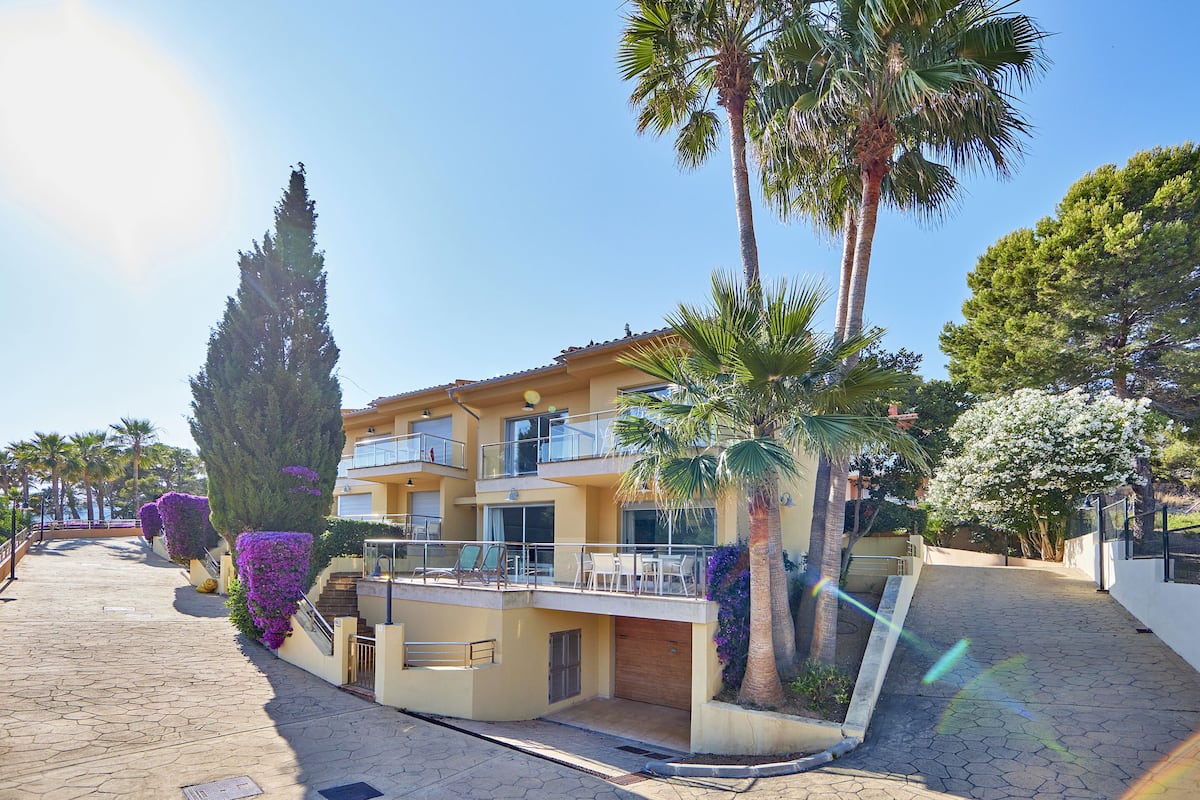 A multi-story building with balconies, palm trees, and a paved walkway.