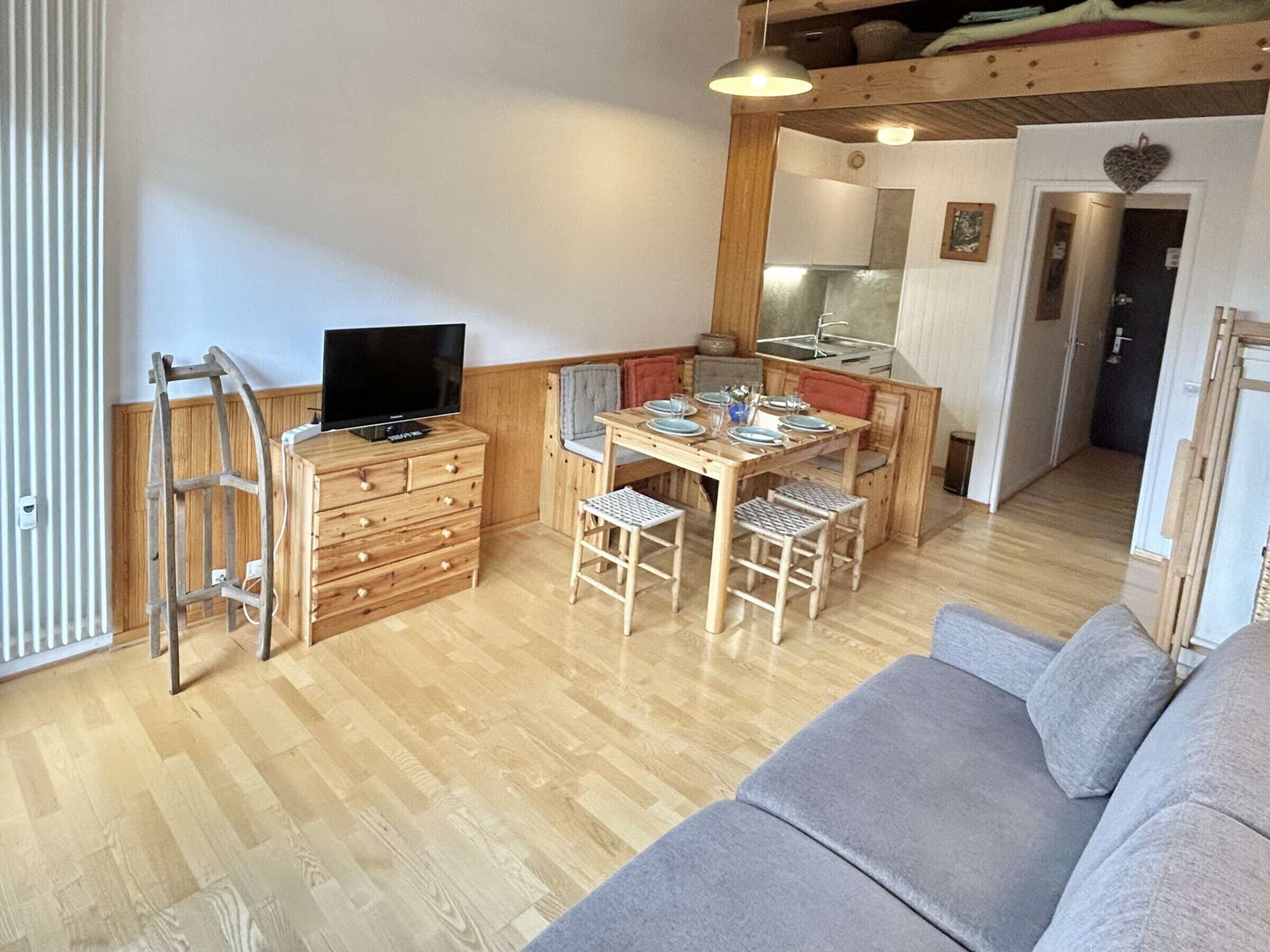 A cozy living area with a wooden dining table set for four, a sofa, and a TV on a wooden dresser.