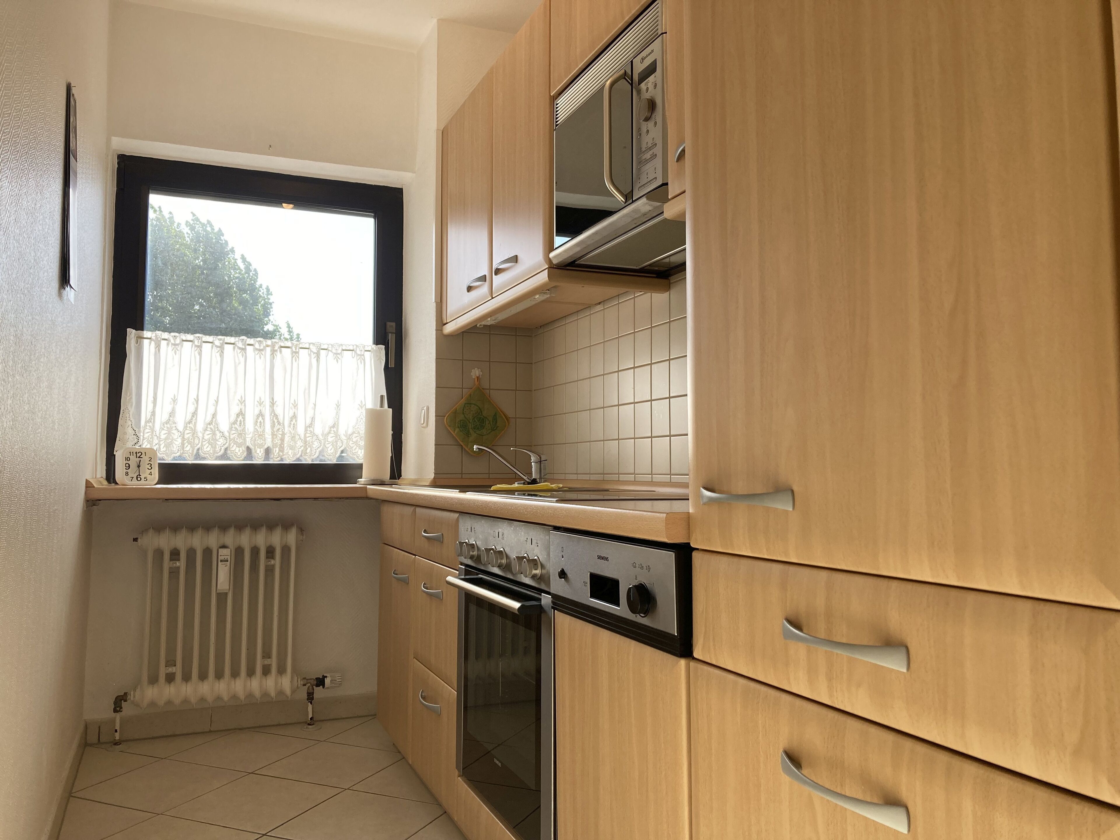 Una cocina compacta con armarios de madera, horno integrado, microondas y una ventana con cortina.