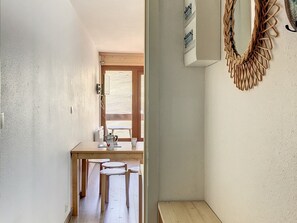 A narrow hallway with a wooden table and two stools, leading to a window with a view of a building.