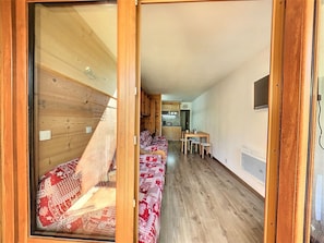 A compact, well-lit room with a wooden floor, a kitchenette, and a dining area with a table and chairs.