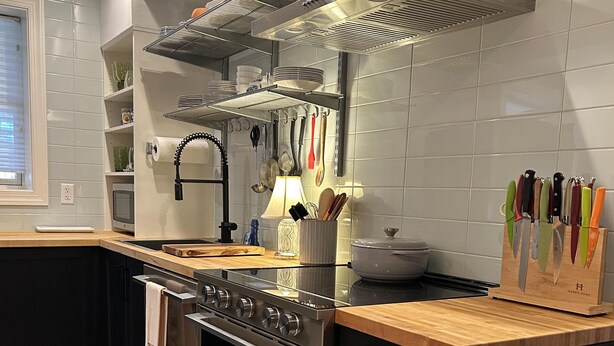 Una cocina moderna con electrodomésticos de acero inoxidable, encimera de madera y diversos utensilios colgados en la pared.