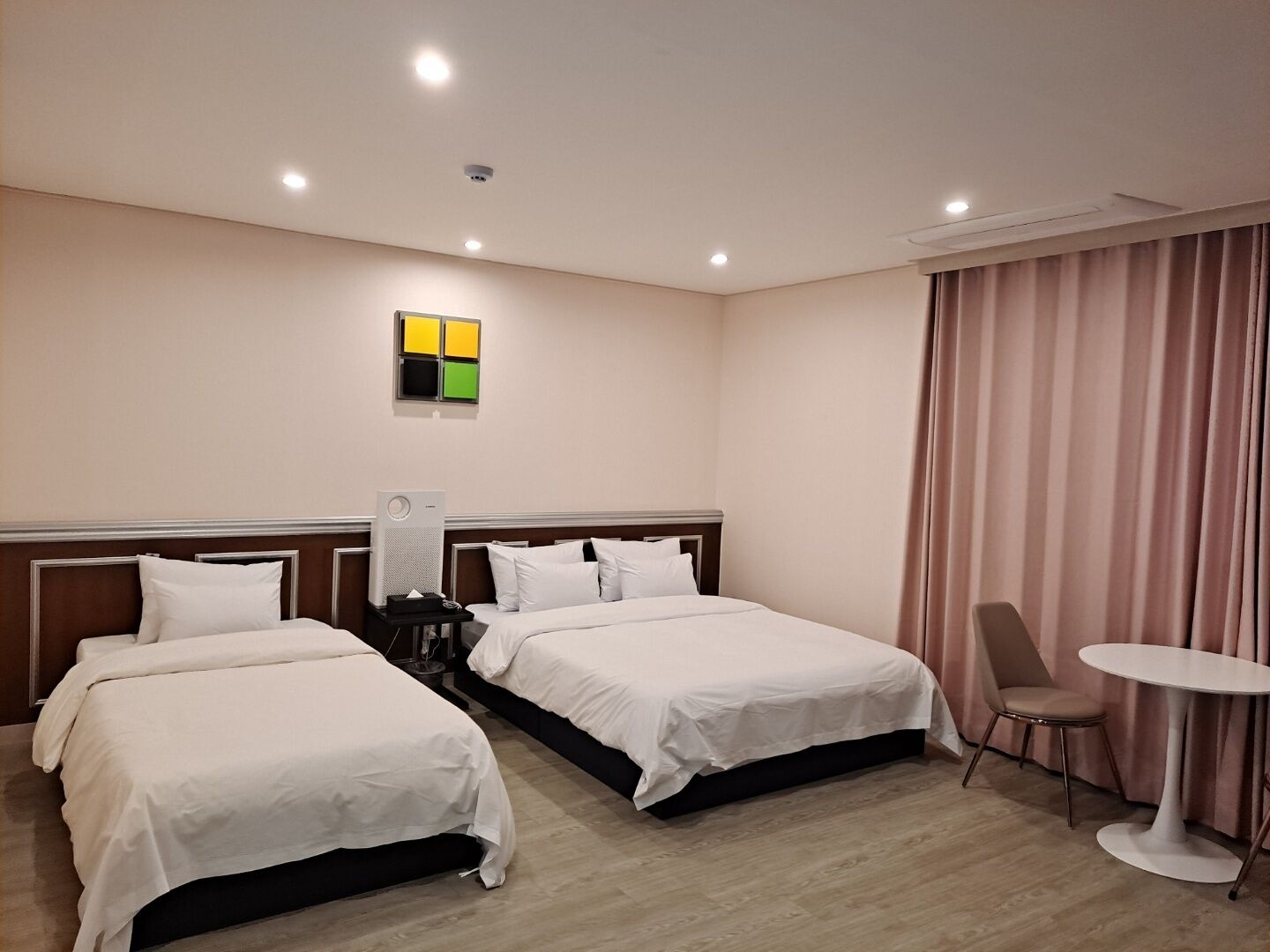 Une chambre d’hôtel avec deux lits, une petite table, une chaise et un panneau de commande fixé au mur.