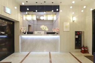 Zona de recepción de un hotel con mostrador de mármol, iluminación colgante moderna y panel de alarma contra incendios.