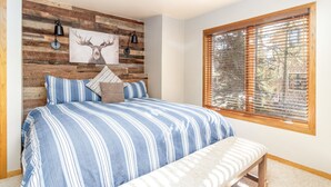 A bedroom with a bed, bench, wooden wall paneling, a deer painting, and a window with blinds. - Private Hot Tub. Steps to The Lift. Beautiful Home (Breckenridge)