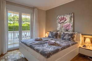 Ein Schlafzimmer mit einem großen Bett, einem Bild an der Wand und Blick ins Grüne.
