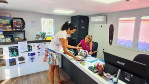 A reception desk with a computer, a magazine rack, and a bulletin board with various notices. - Camping Tikayan Les Palmiers (Hyères)