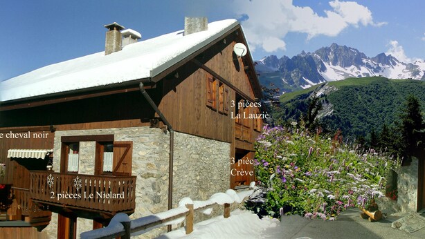 Eine Holzhütte mit Steinverkleidung, einem Balkon und Blick auf verschneite Berge.