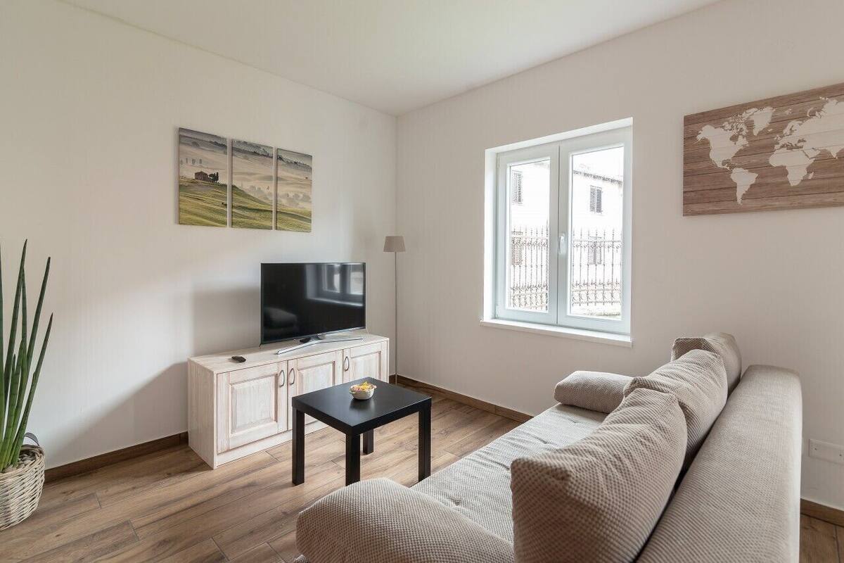 A living room with a sofa, a TV on a cabinet, a small table, and a window with a view.