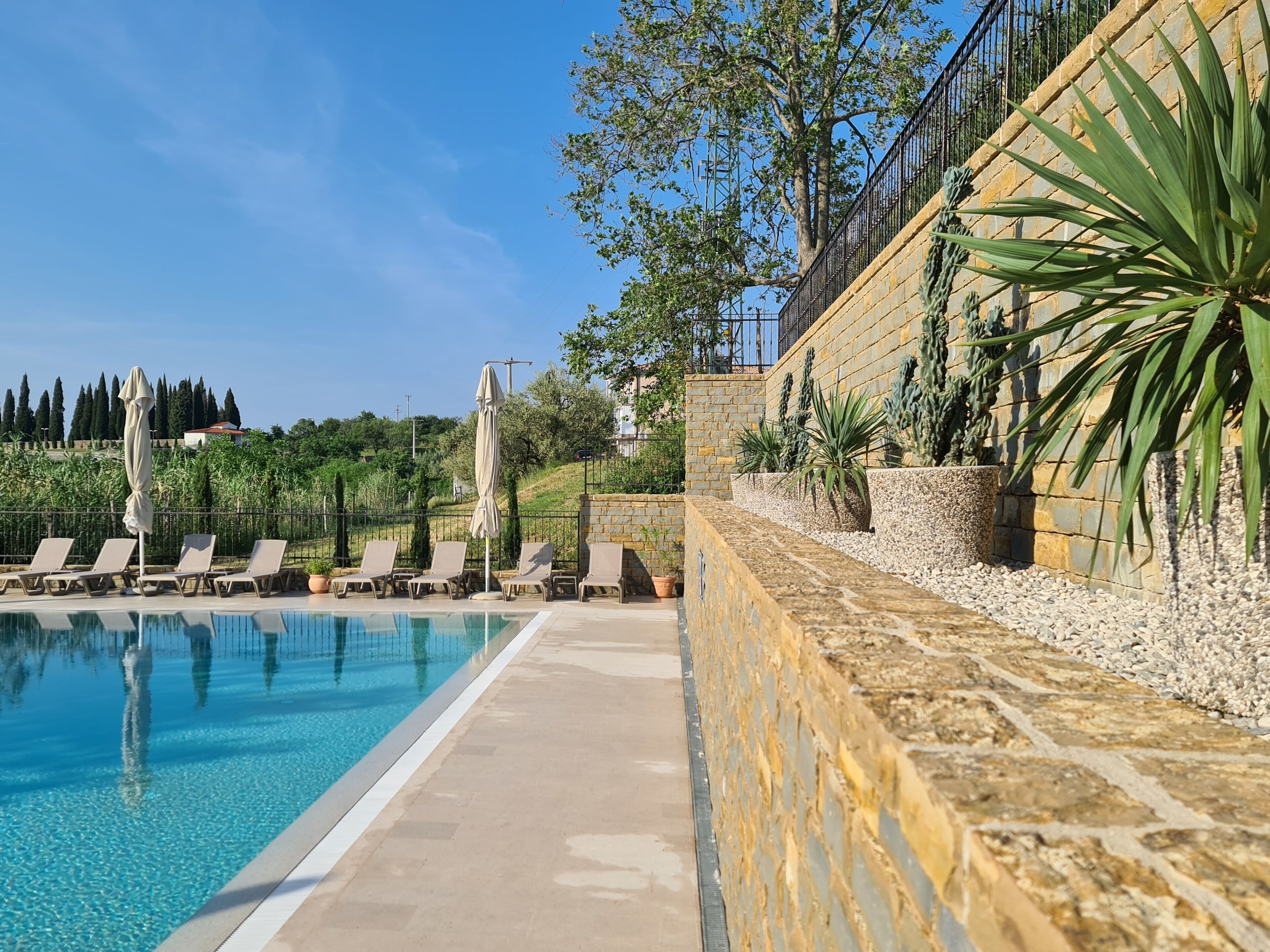 Une piscine entourée de murs de pierre et de verdure, avec des chaises longues et des parasols.