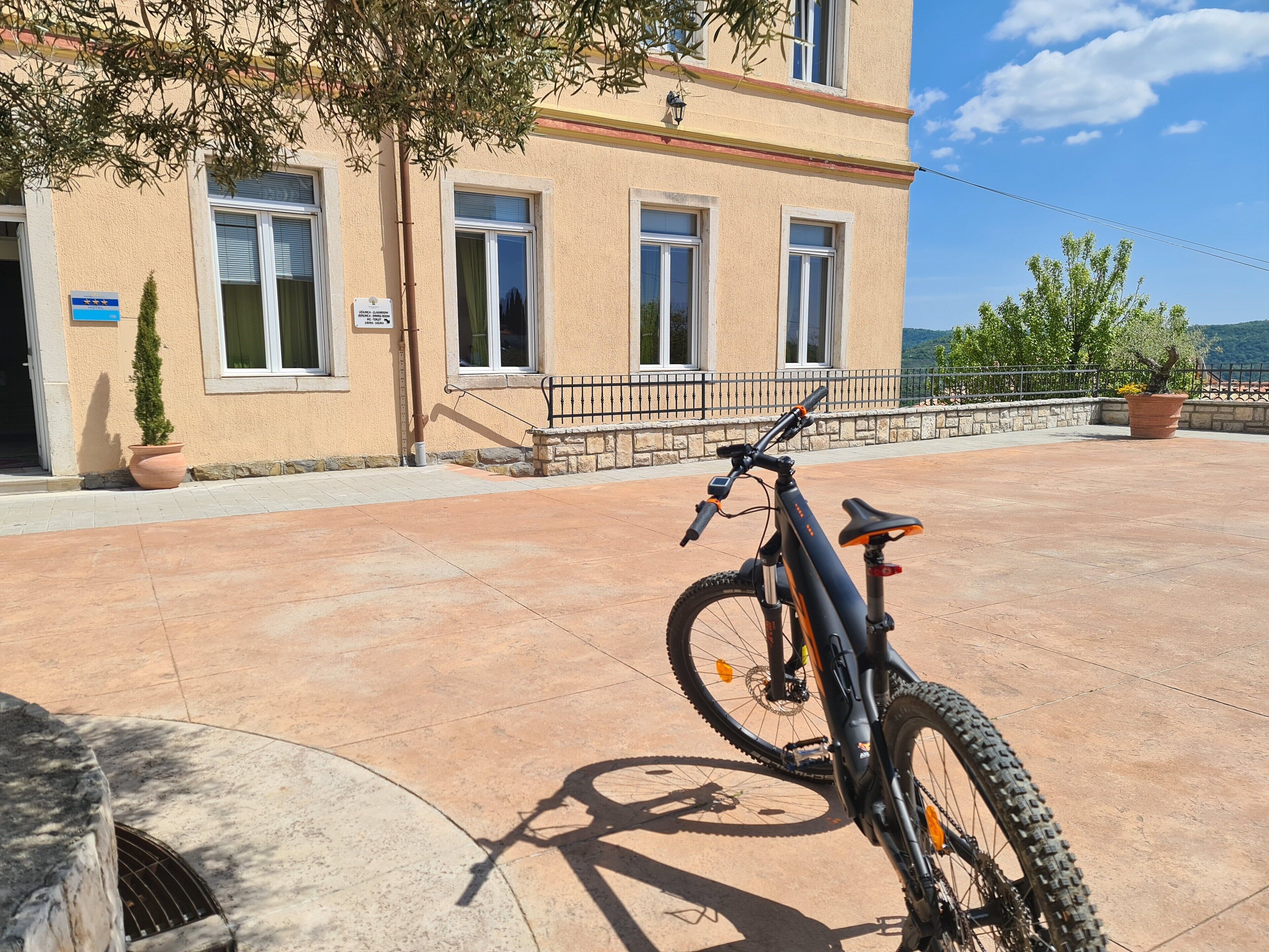 A building with a paved terrace, a bicycle, and a sign indicating a location.
