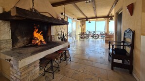 Un intérieur rustique avec une cheminée en pierre, des poutres en bois et une vue sur l’extérieur.