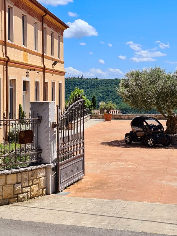 A large building with a gated entrance, a paved courtyard, and a car parked nearby. - Residence Stara šola Korte - Oleander Resort (Izola)