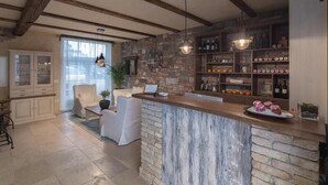 Une cuisine dotée d’un îlot central en pierre, de poutres apparentes en bois et d’un coin bar avec des étagères remplies de bouteilles et de bocaux.