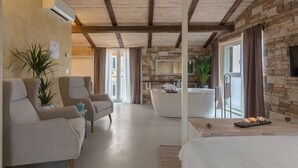 Une chambre d’hôtel moderne avec un mur en pierre, une grande baignoire et un coin salon comprenant deux fauteuils et une table d’appoint.