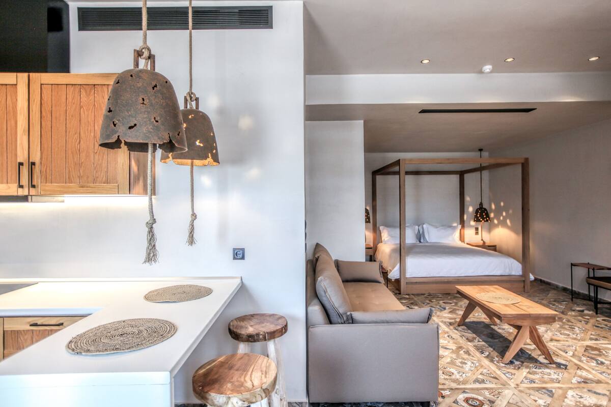 A modern hotel room with a wooden bed frame, a sofa, a small table, and a unique ceiling design.